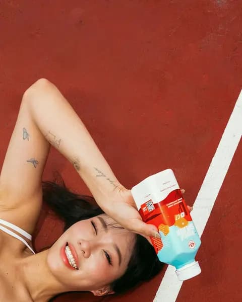 A woman lying on a tennis court, laughing, a C7 Tropical Splash resting on the forehead