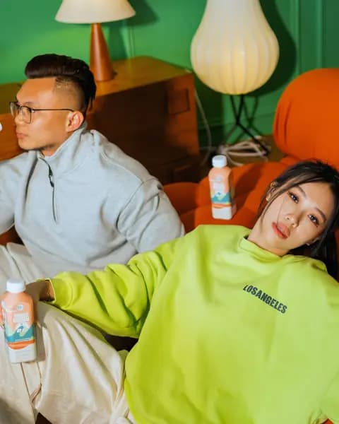 A woman in a lime sweatshirt leaning on an orange sofa with a C7 Almond Oasis, a friend alongside